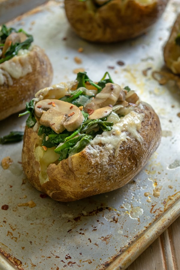 Spinach Mushroom Stuffed Baked Potatoes with Cheddar dripping down the side on a sheet pan