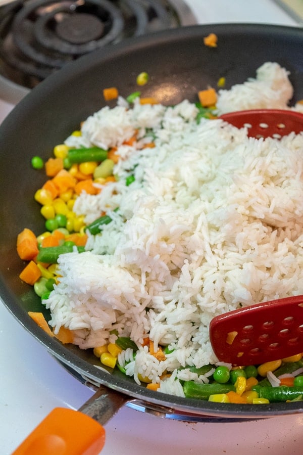 vegetables and rice being tossed in the skillet