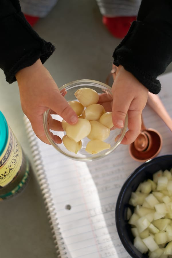 toddler hands holding a bowl of garlic ready for the crockpot