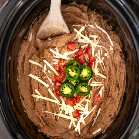 Easy Vegetarian Crockpot Refried Beans with cheese, tomatoes, and jalapeños with a spoon for scooping