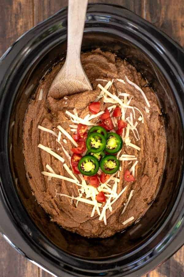 Easy Vegetarian Crockpot Refried Beans with cheese, tomatoes, and jalapeños with a spoon for scooping