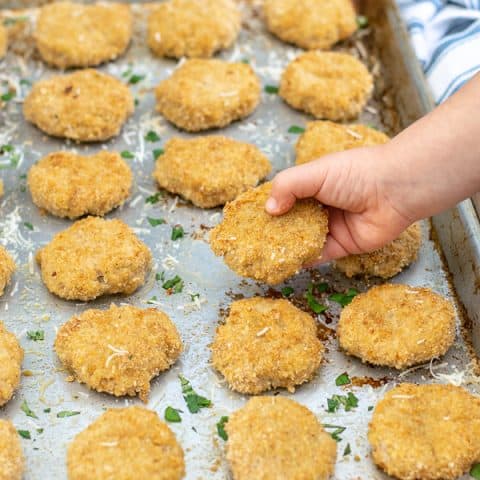 a toddler hand holding a baked chicken nugget