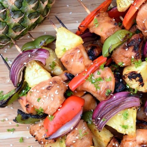Freshly grilled Pineapple Chicken Kabobs on a bamboo board with a pineapple