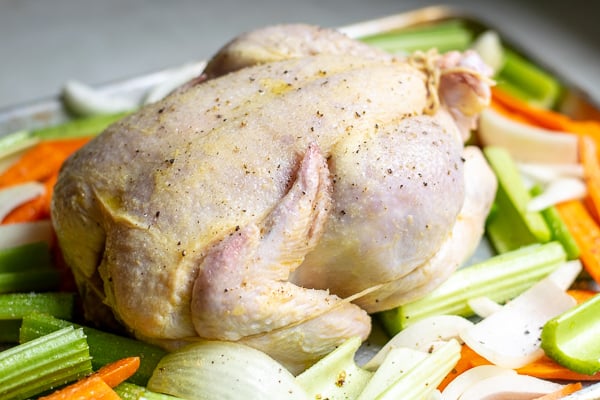 chicken trussed on a sheet pan over a bed of vegetables 
