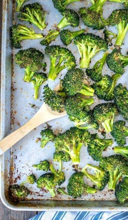 A wooden spoon scooping up oven roasted broccoli on a sheet pan.