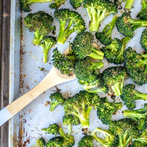 A wooden spoon scooping up oven roasted broccoli on a sheet pan.