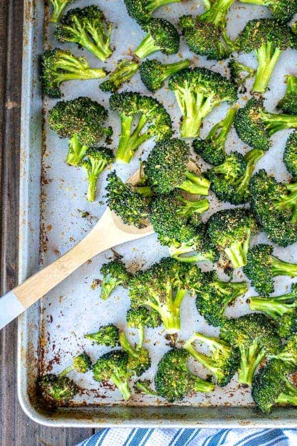 A wooden spoon scooping up oven roasted broccoli on a sheet pan.