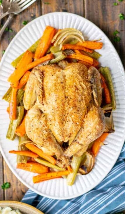 whole roasted chicken on a bed of veggies on a white platter
