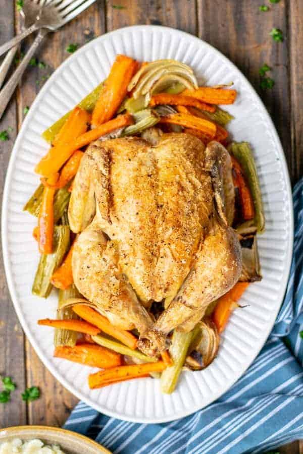 whole roasted chicken on a bed of veggies on a white platter