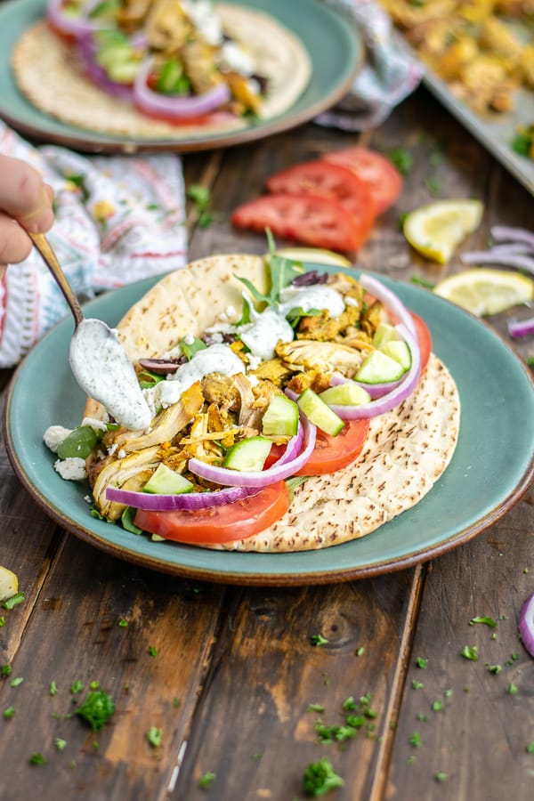 a spoon drizzling tzatziki sauce over a chicken shawarma pita