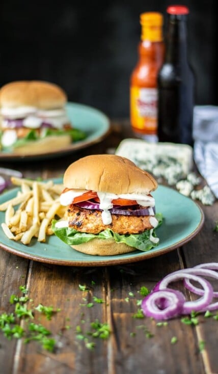 a stuffed chicken burger on a teal plate with French fries on a table