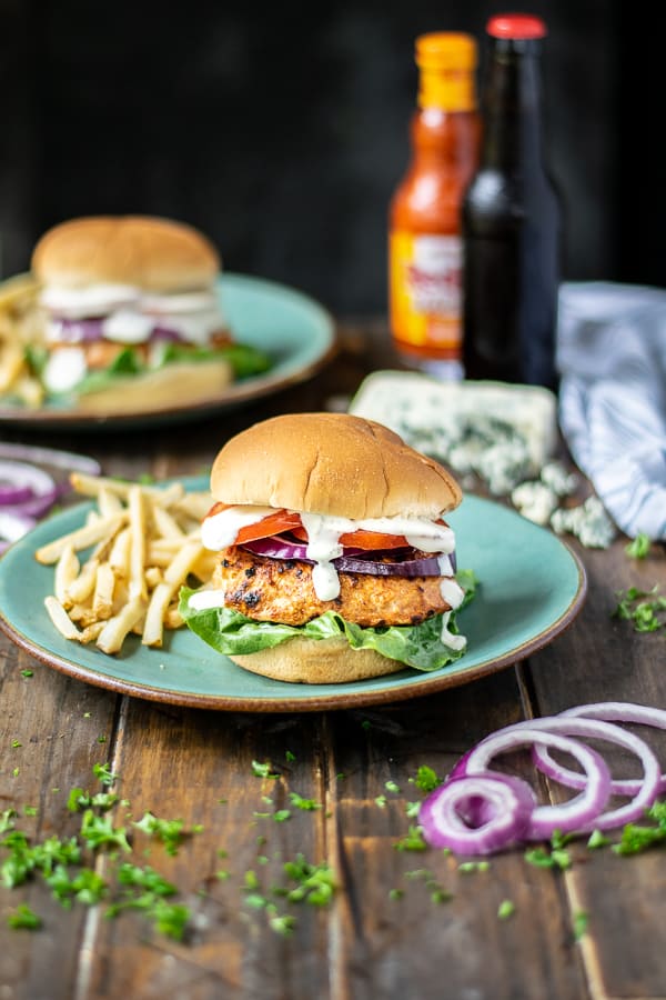 a stuffed chicken burger on a teal plate with French fries on a table