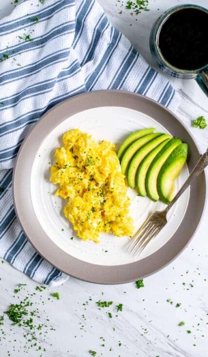 cottage cheese scrambled eggs and sliced avocado on a plate with a fork