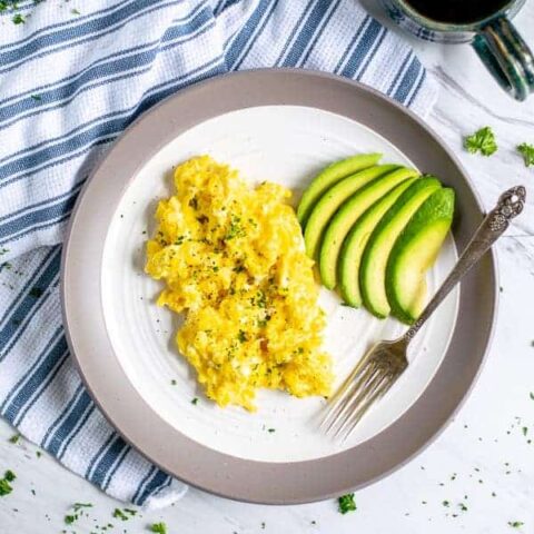 cottage cheese scrambled eggs and sliced avocado on a plate with a fork