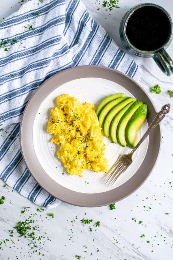 cottage cheese scrambled eggs and sliced avocado on a plate with a fork