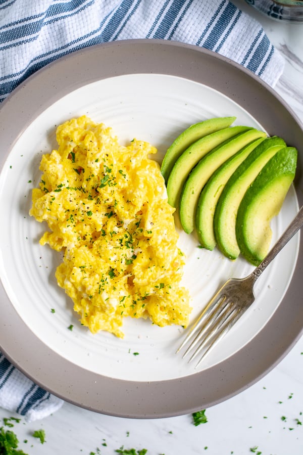 overhead shot of scrambled eggs on a plate with sliced avocados and a fork