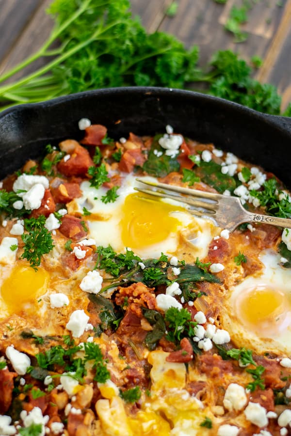 a fork in the runny yolk of an egg in the shakshuka