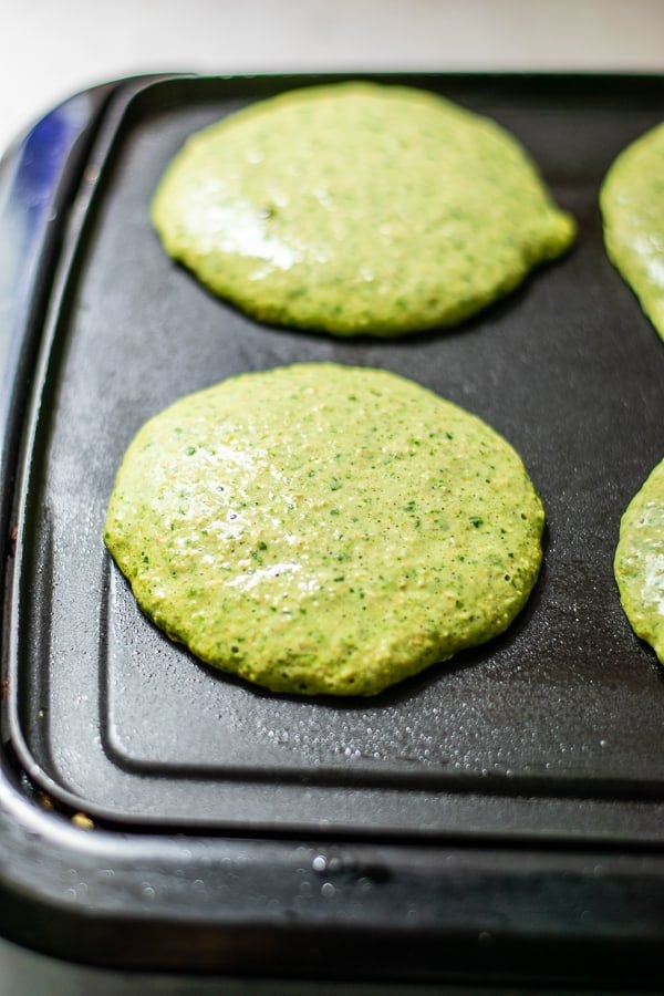 green pancakes being cooked on a black griddle