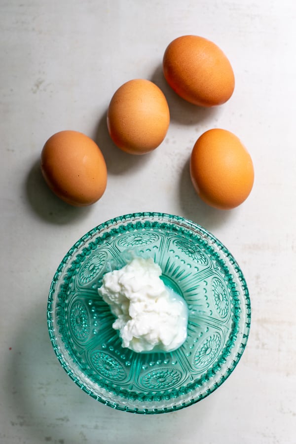 cottage cheese in a blue bowl with 4 brown eggs next to it on a counter
