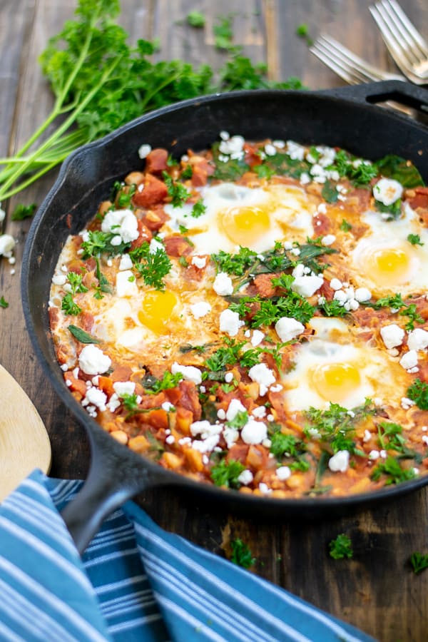 skillet of shakshuka with beans on a table with parsley and feta