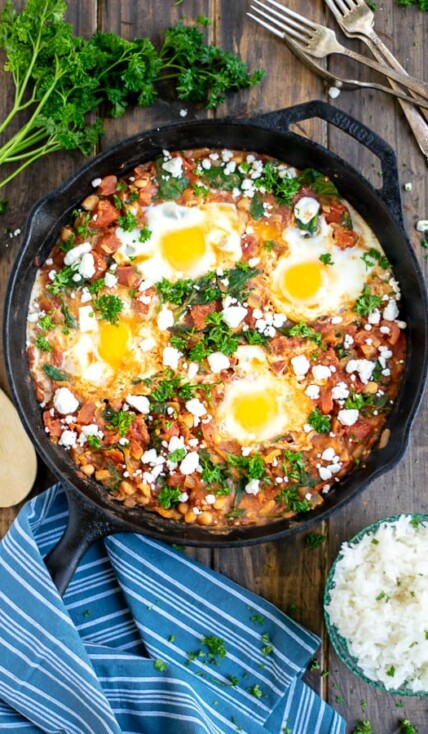 overhead shot of shakshuka in a cast iron skillet on a wood table with a blue striped towel