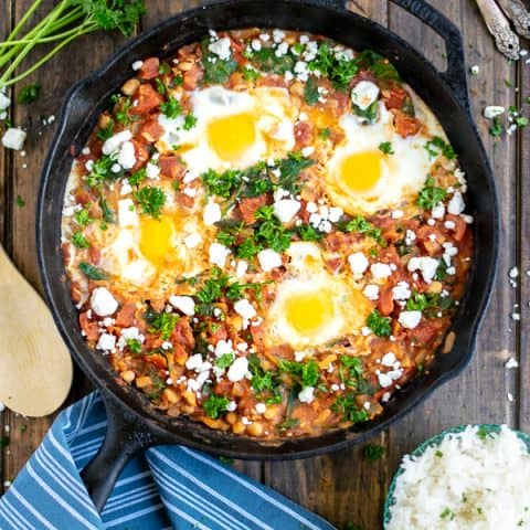 overhead shot of shakshuka in a cast iron skillet on a wood table with a blue striped towel