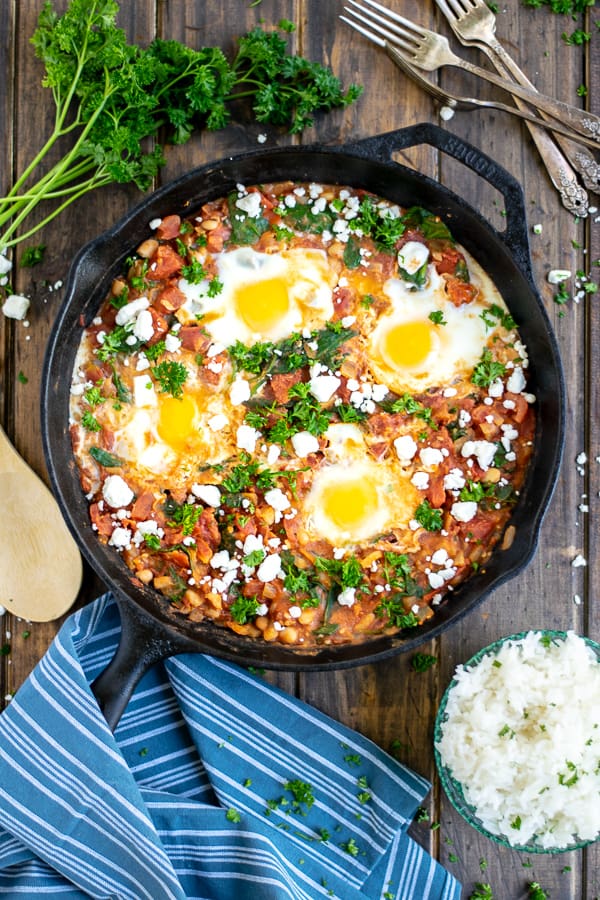 overhead shot of shakshuka in a cast iron skillet on a wood table with a blue striped towel