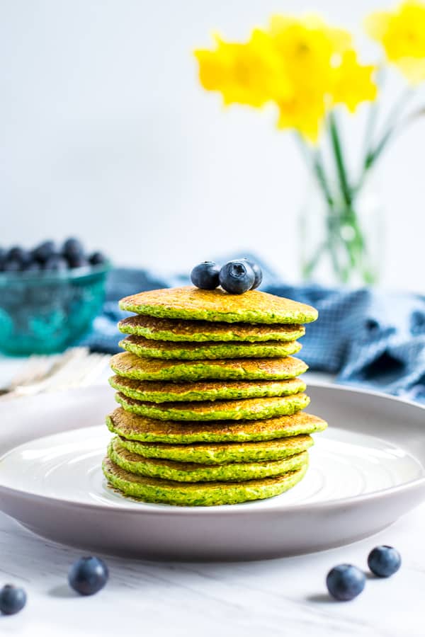 stack of green spinach oatmeal pancakes on a white plate topped with blueberries