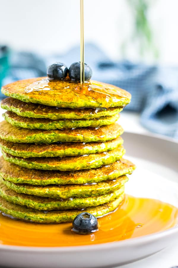 Stack of Spinach Pancakes on a plate with blueberries on top and syrup being drizzled over the top