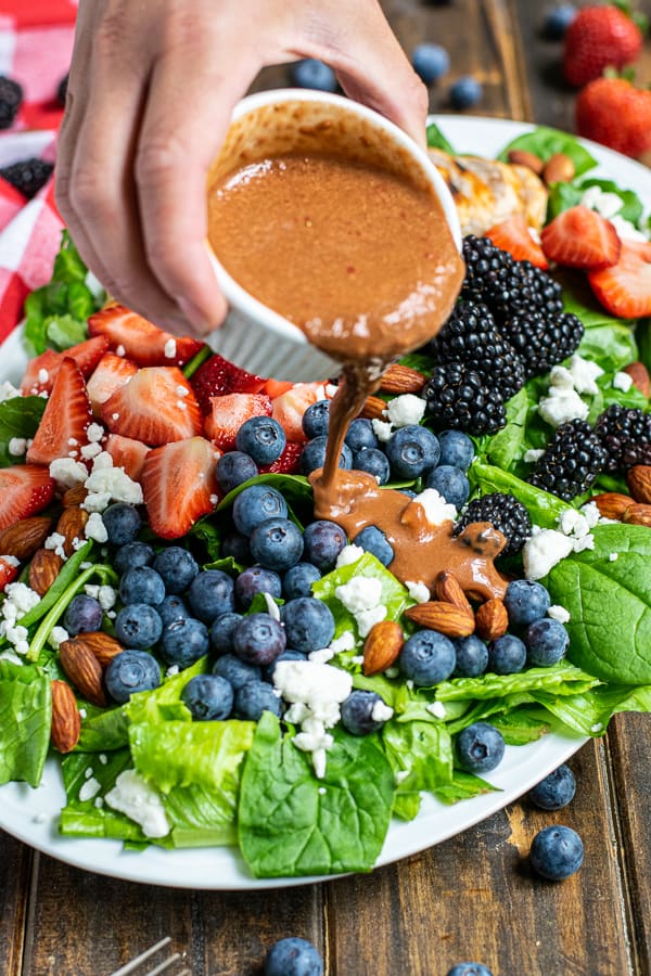 strawberry balsamic vinaigrette being poured on to a summery berry salad