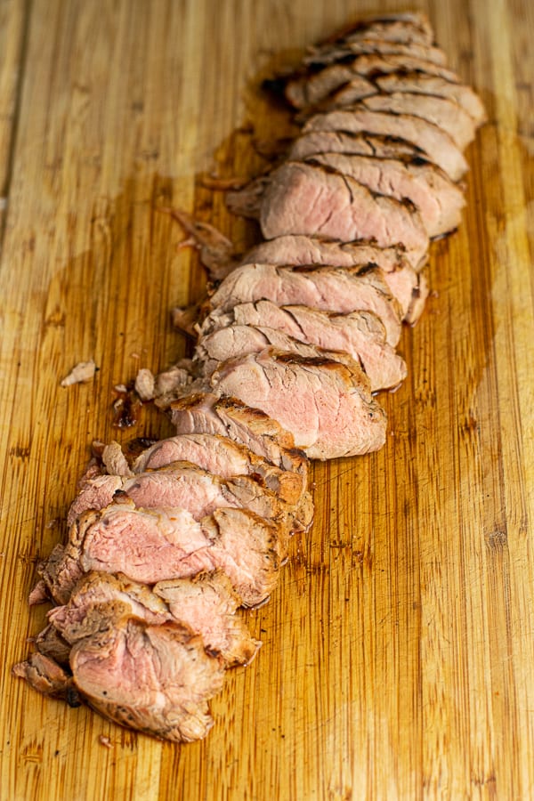 a pork tenderloin sliced open reveling a slightly pick center on a cutting board