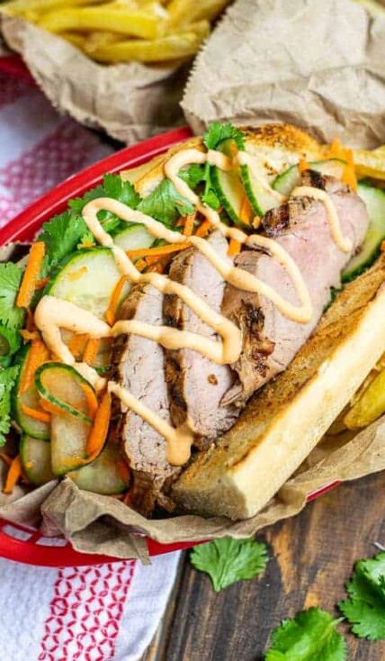 a flavorful grilled pork banh mi in a serving basket with quick pickled vegetables, sriracha mayo, and cilantro