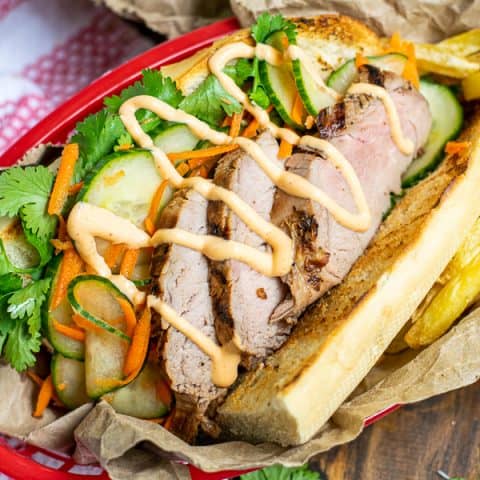 a flavorful grilled pork banh mi in a serving basket with quick pickled vegetables, sriracha mayo, and cilantro