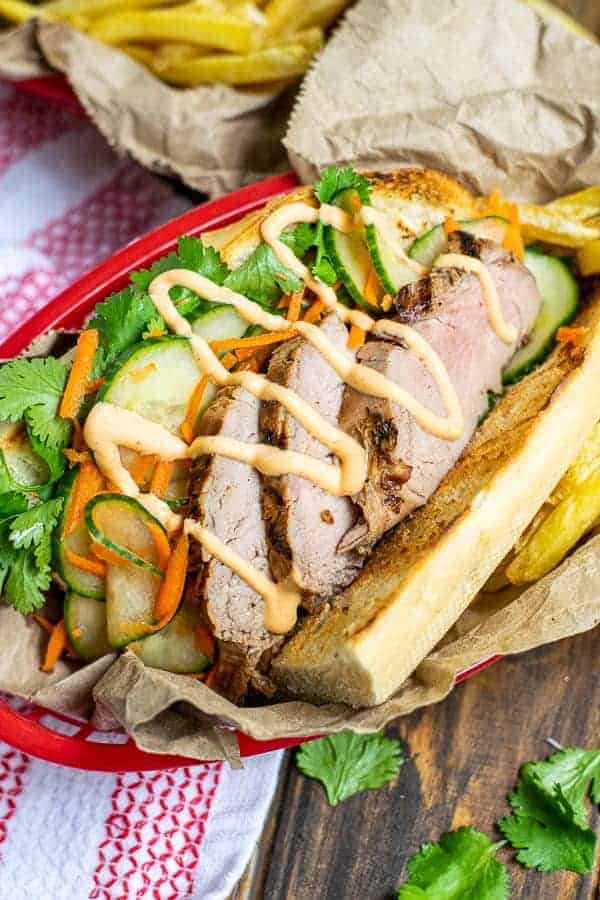 a flavorful grilled pork banh mi in a serving basket with quick pickled vegetables, sriracha mayo, and cilantro