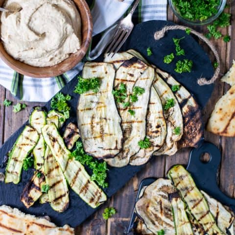 a spread of grilled zucchini, eggplant, naan, and hummus over a wooden background