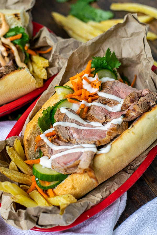 garlic lime mayo drizzled over a banh mi in a serving basket with French fries
