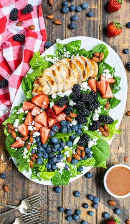 overhead view of a summer berry salad on a large platter with a napkin and a lot of berries