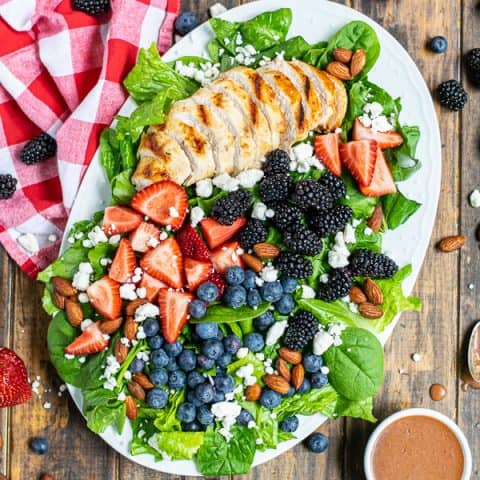 overhead view of a summer berry salad on a large platter with a napkin and a lot of berries