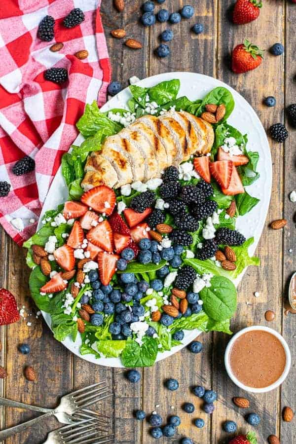 overhead view of a summer berry salad on a large platter with a napkin and a lot of berries