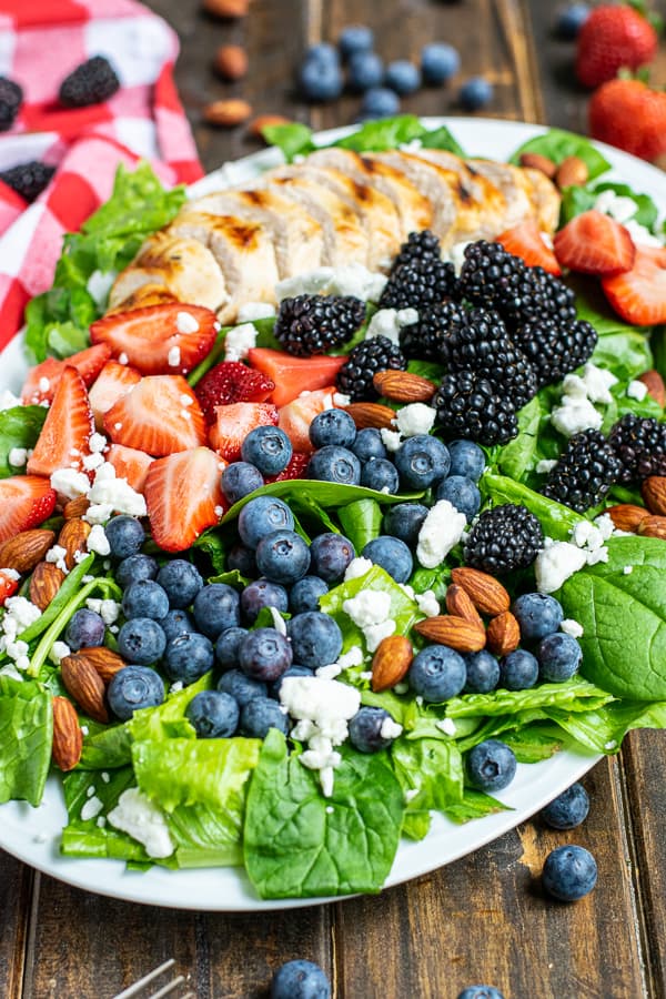 three different kinds of berries with grilled chicken on top of fresh salad greens with almonds and feta cheese on a large platter