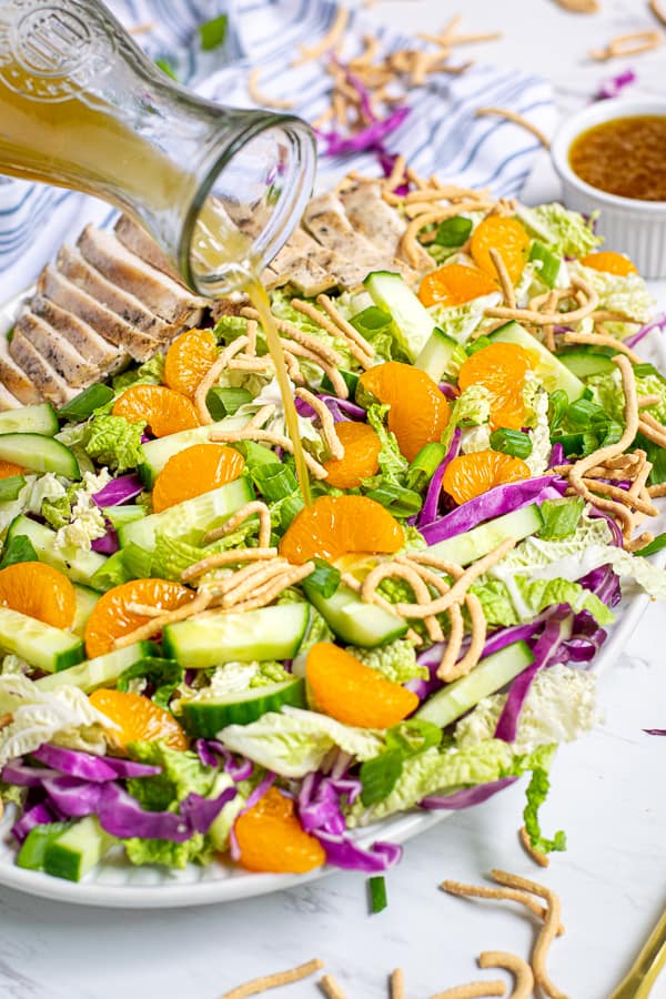 sesame vinaigrette being poured onto a plate full of asian chopped salad