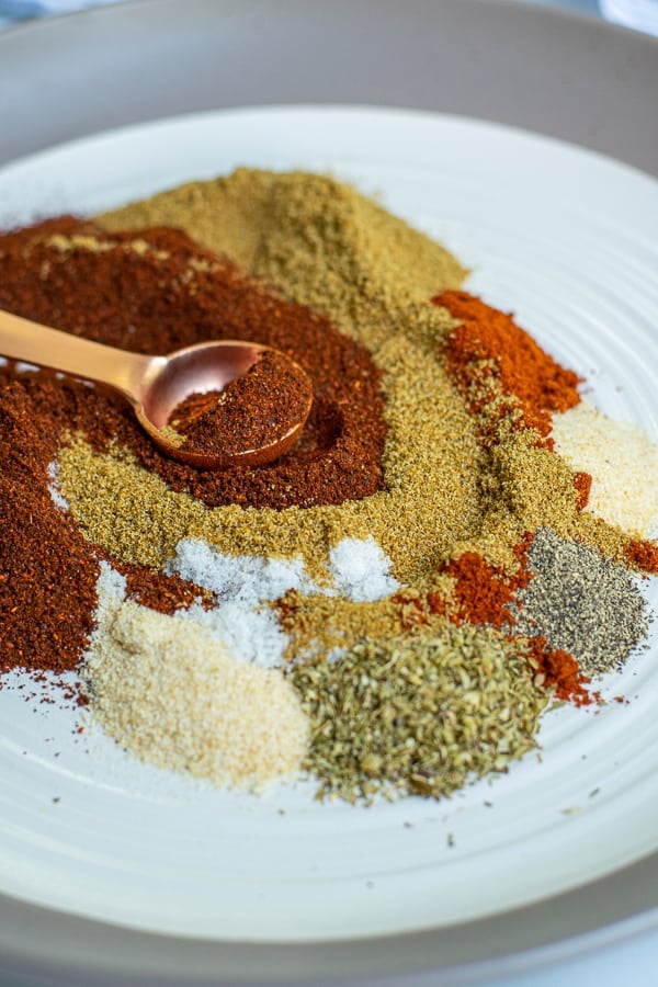 spoon swirling together spices for the taco seasoning on a white plate