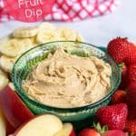 bowl of peanut butter yogurt fruit dip sitting on a platter filled with sliced fruits
