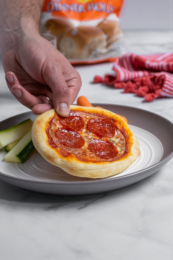 adult hand grabbing a personal pizza off of a white plate