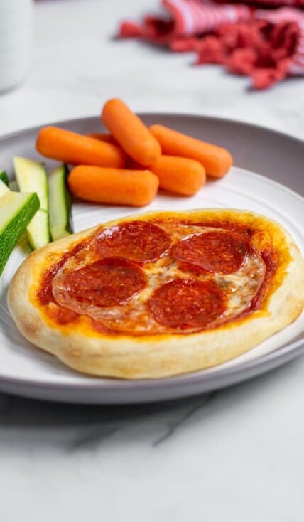 Close up of individual pizza on a plate with vegetables perfect for a weeknight dinner.