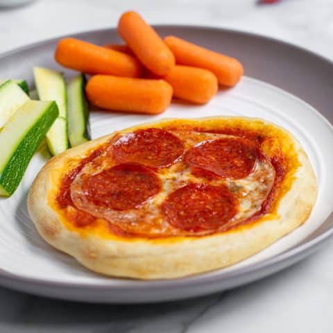 Close up of individual pizza on a plate with vegetables perfect for a weeknight dinner.