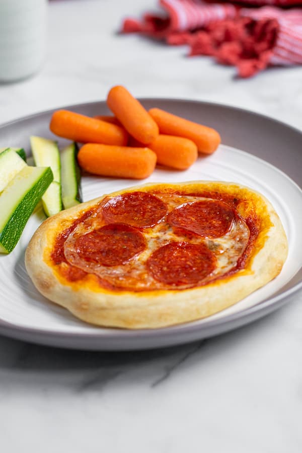 Close up of individual pizza on a plate with vegetables perfect for a weeknight dinner.