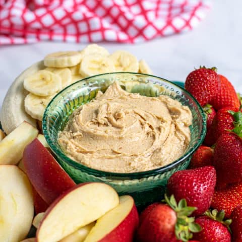 Platter with peanut butter fruit dip surrounded by cut up fruit.