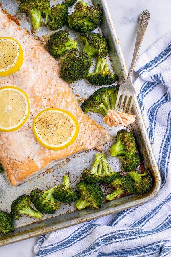Forkful of baked salmon with broccoli on a sheet pan.