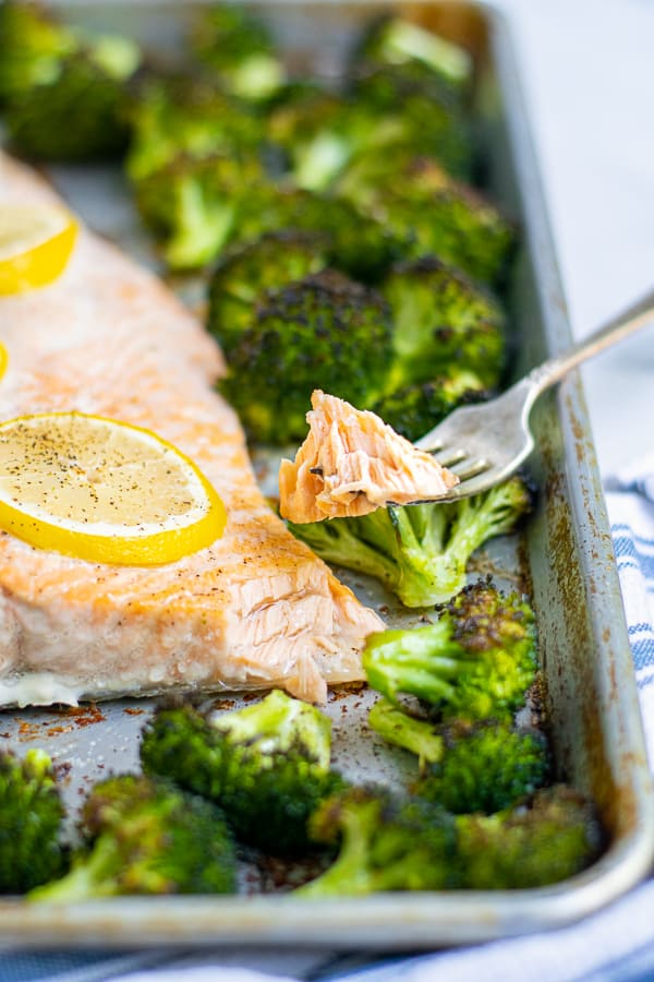 bite of cooked salmon on a fork resting on a sheet pan of salmon and broccoli 